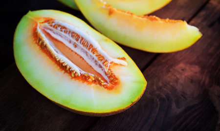 Ripe juicy melon cut in half on a brown wooden background, close upの写真素材