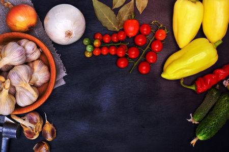 Fresh vegetables: tomatoes, cucumbers and garlic on a black background, empty space in the middleの写真素材