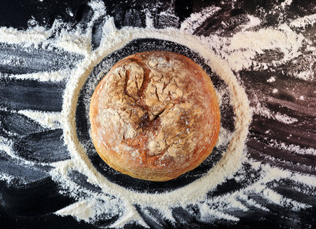 round baked bread and white wheat flour scattered on a black table, top viewの写真素材