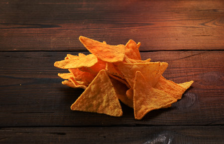 pile of corn tortilla chips or nachos on a brown wooden background, close upの写真素材