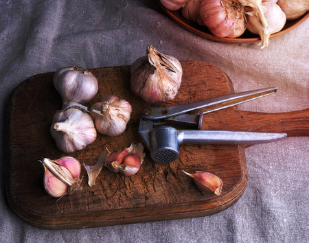 raw unpeeled garlic on a very old vintage cutting board and an iron extruder for a product, dark backgroundの写真素材