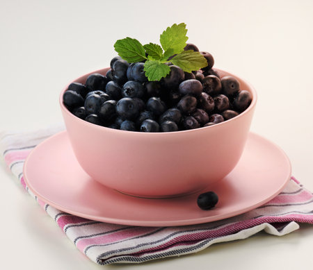Ripe blueberry in a pink ceramic plate on a white table, tasty and useful berryの写真素材
