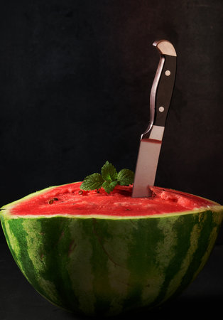 ripe red watermelon, stuck in a large knife. Black backgroundの写真素材