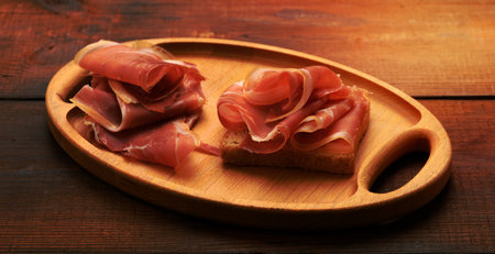 sandwich with a white square slice of bread and slices of prosciutto on a wood boardの写真素材