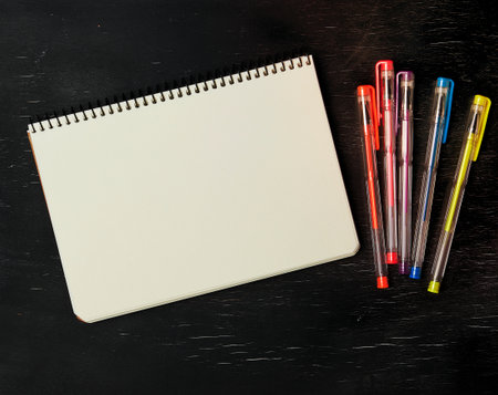 open notebook and gel pen on a black wooden background, top view, empty white sheetsの写真素材