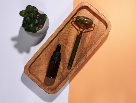 Hand held face massager and brown glass bottle with dropper on marble plate, top viewの写真素材