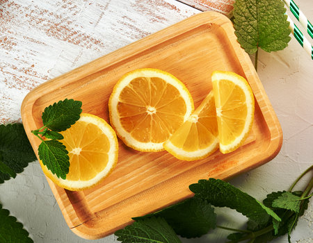sliced yellow juicy lemon slices on a wooden board and green fresh mint leaves, top viewの写真素材