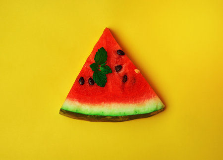 triangular slice of ripe red watermelon with seeds on a yellow background, close upの写真素材