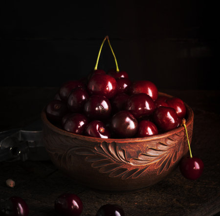 ripe red juicy sweet cherry in a brown clay bowl on a wooden tableの写真素材