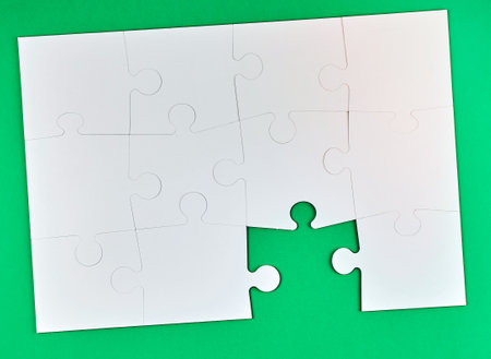 game of puzzles made of white paper pieces interconnected on a green background, one element is missing, top viewの写真素材