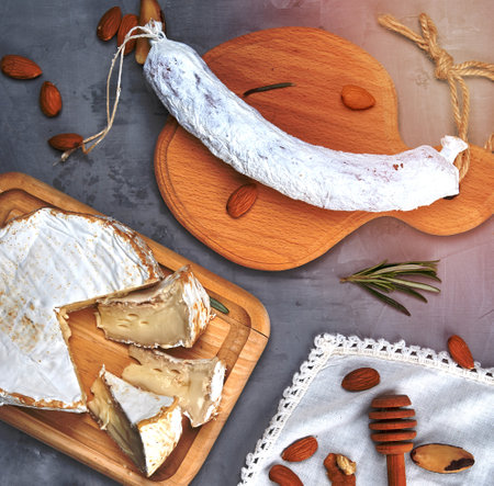 round piece of brie cheese and sausage on a wooden board, gray background, top viewの写真素材