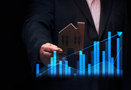 hand holds a wooden model of a house on a dark background. Real estate sale and purchase concept, rise in property pricesの写真素材