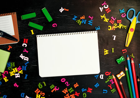 open spiral notebook with clean white sheets, wooden colored pencils, scissors on a black background, back to school backdropの写真素材