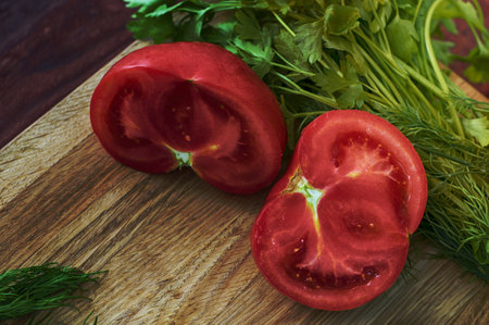 Slices of tomato on a wooden board with dill and parsleyの写真素材