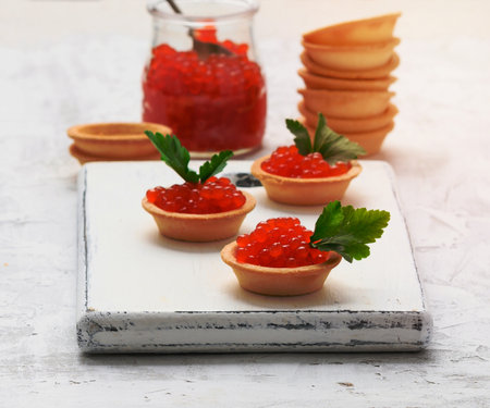 red chinook caviar in a glass jar and round tartlets on a white table, close upの写真素材