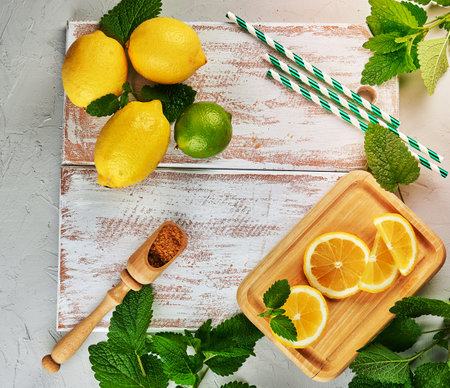 ripe yellow whole lemons and lime, brown sugar and a bunch of fresh mint on a white wooden board, ingredients for lemonade, top viewの写真素材