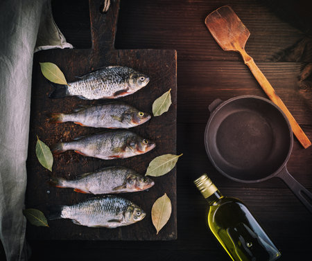 river fish on brown wooden board, beside an empty round black cast-iron panの写真素材