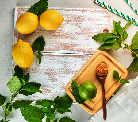 ripe yellow whole lemons and lime, brown sugar and a bunch of fresh mint on a white wooden board, ingredients for lemonade, copy spaceの写真素材