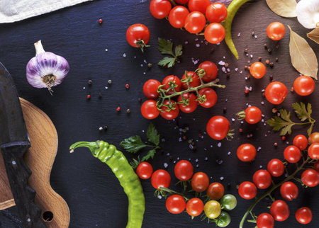 Ripe red cherry tomatoes, chili and spices on a black background, close upの写真素材