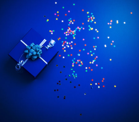 square blue shiny box with a bow and multicolored sparkles on a blue background, top view. Valentine giftの写真素材