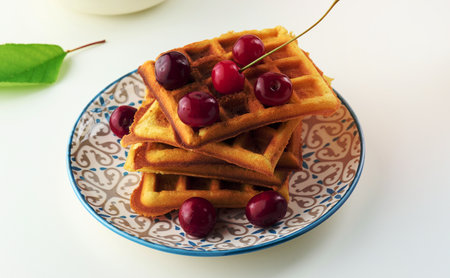 Stack of baked Belgian waffles with ripe red cherries on the white table, breakfastの写真素材
