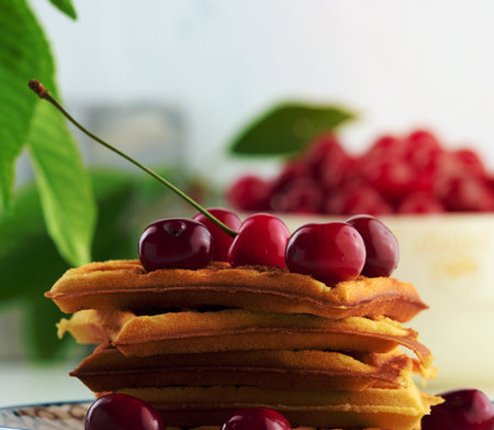 Stack of baked Belgian waffles with ripe red cherries on the white table, breakfastの写真素材