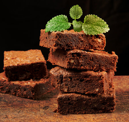 stack of baked square pieces of chocolate brownie cake on brown wooden cutting board, black backgroundの写真素材