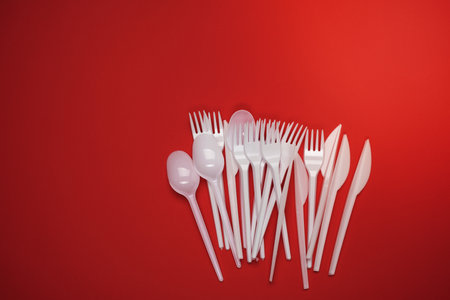stack of plastic forks and spoons on red background, top view, copy spaceの写真素材