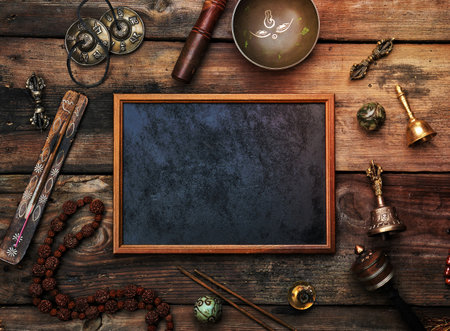 Empty wooden frame and copper singing bowl, prayer beads, prayer drum and other Tibetan religious objects for meditation and alternative medicine on a brown wooden background, copy spaceの写真素材