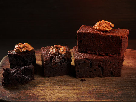 stack of baked pieces of brownie chocolate cake with nuts on a wooden board, delicious dessert, close upの写真素材