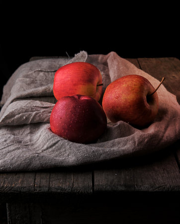 three fresh red apples lay on gray linen napkin, dark backgroundの写真素材