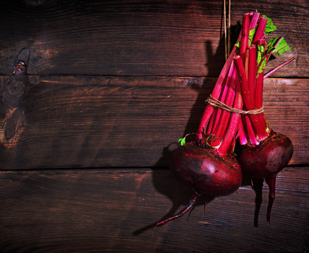 Two fresh red beets hang on a rope on a wooden wallの写真素材