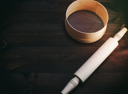 wooden rolling pin and  a wooden round sieve on a brown table, top view, empty spaceの写真素材