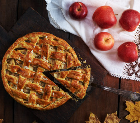baked traditional fruit cake on a brown wooden board and fresh apples on a white textile napkinの写真素材