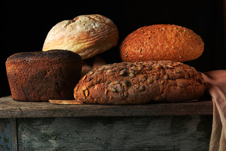 whole various baked rye flour bread rolls on an old wooden table, black backgroundの写真素材