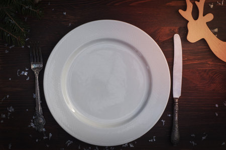 White plate with silver knife and fork on brown wooden surface Christmas table setting, top viewの写真素材