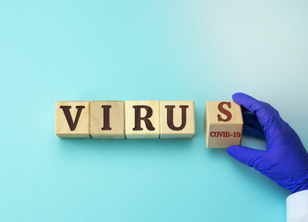 wooden cubes with the inscription Virus. Doctor's hand holds a cube. Coronavirus 19 epidemic and pandemic spread concept, top viewの写真素材
