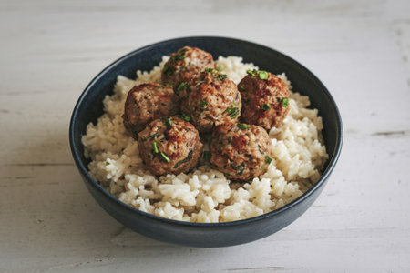 a bowl filled with cooked creamy white rice and meatballsの写真素材