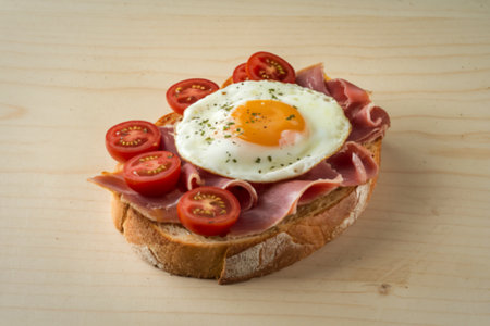 a plate with toast bread with a cooked egg, slices of ham, and cherry tomatoes.の写真素材