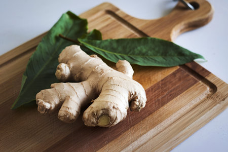a fresh ginger root with leaves on a cutting boardの写真素材