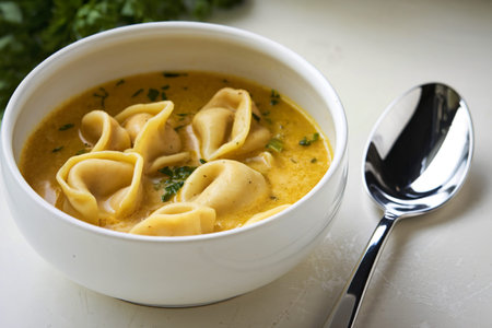 A photo of a white bowl filled with a tortellini soupの写真素材