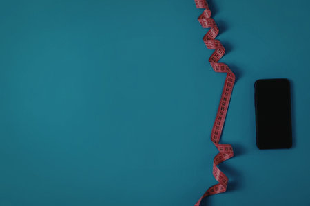 A smartphone lies on a blue surface with a red ribbon beside it.
