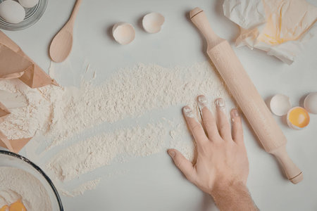 a hand reaching for flour on a kitchen counter with baking ingredients