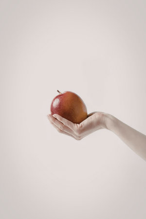 A hand holding a shiny red apple against a white background.