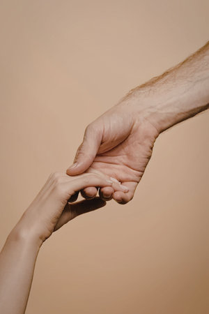 A close-up of two hands holding each other, one larger and one smaller, against a beige background.の写真素材