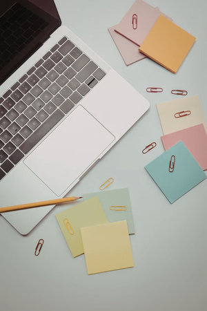 A laptop, sticky notes, paper clips, and a pencil on a deskの写真素材