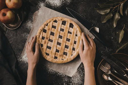 Overhead view of a person's hands handling a lattice-topped pie on a piece of parchment paper,...