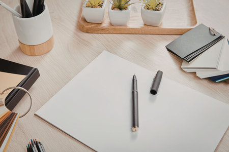 A workspace with a blank sheet of paper, pencils, and notebooks on a wooden desk.