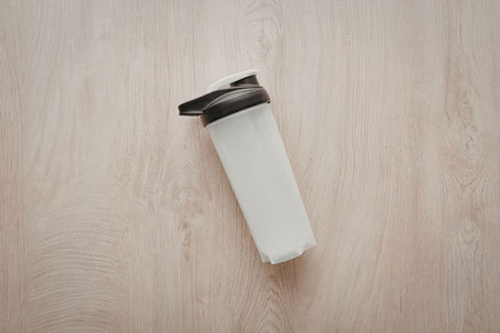 An empty white tube with a black cap lies on a light-colored wooden surface.の写真素材