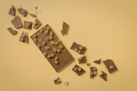A broken chocolate bar with nuts on a yellow background, scattered pieces of chocolate around it.の写真素材